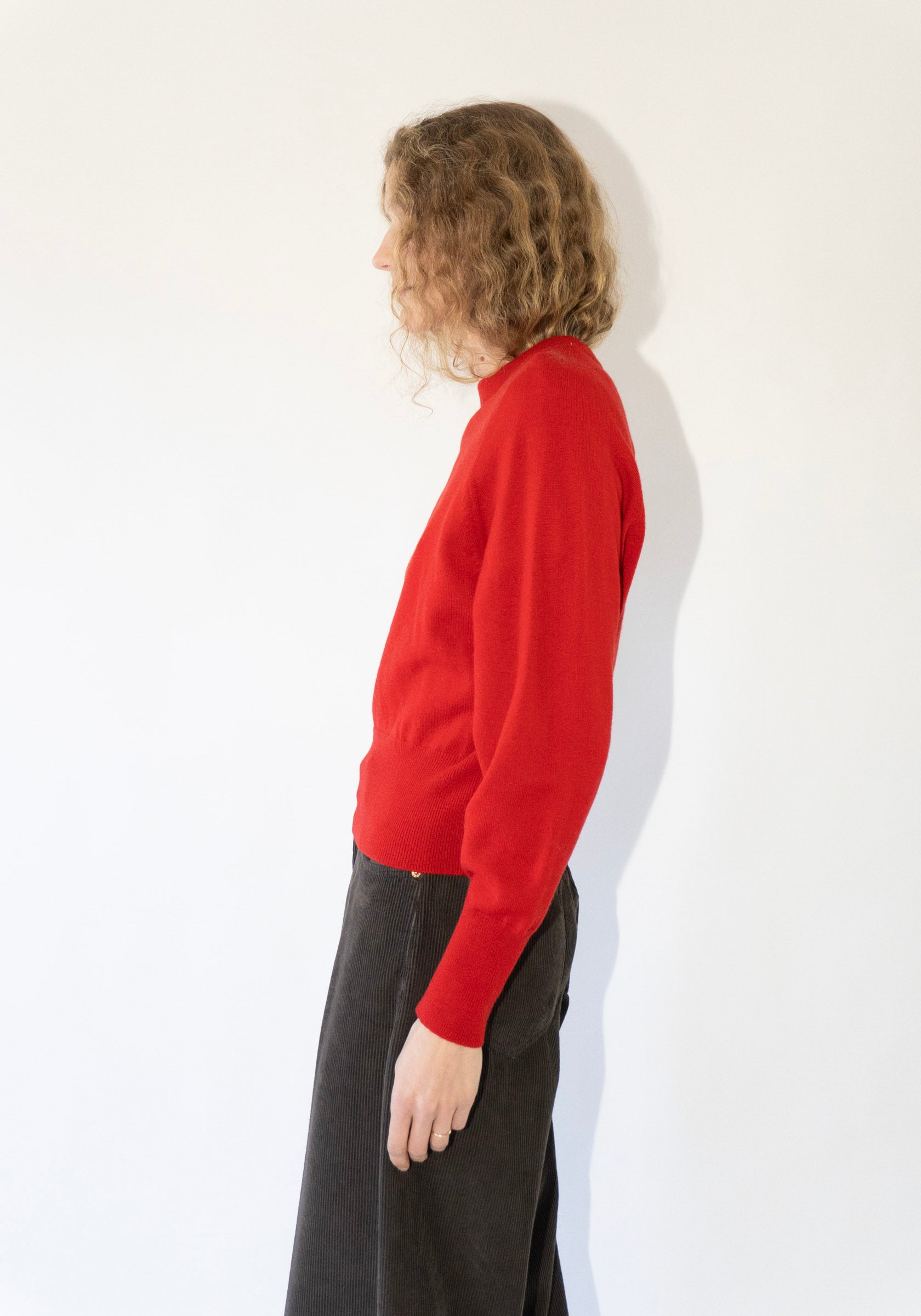 Person wearing a red sweater and dark pants on a white background