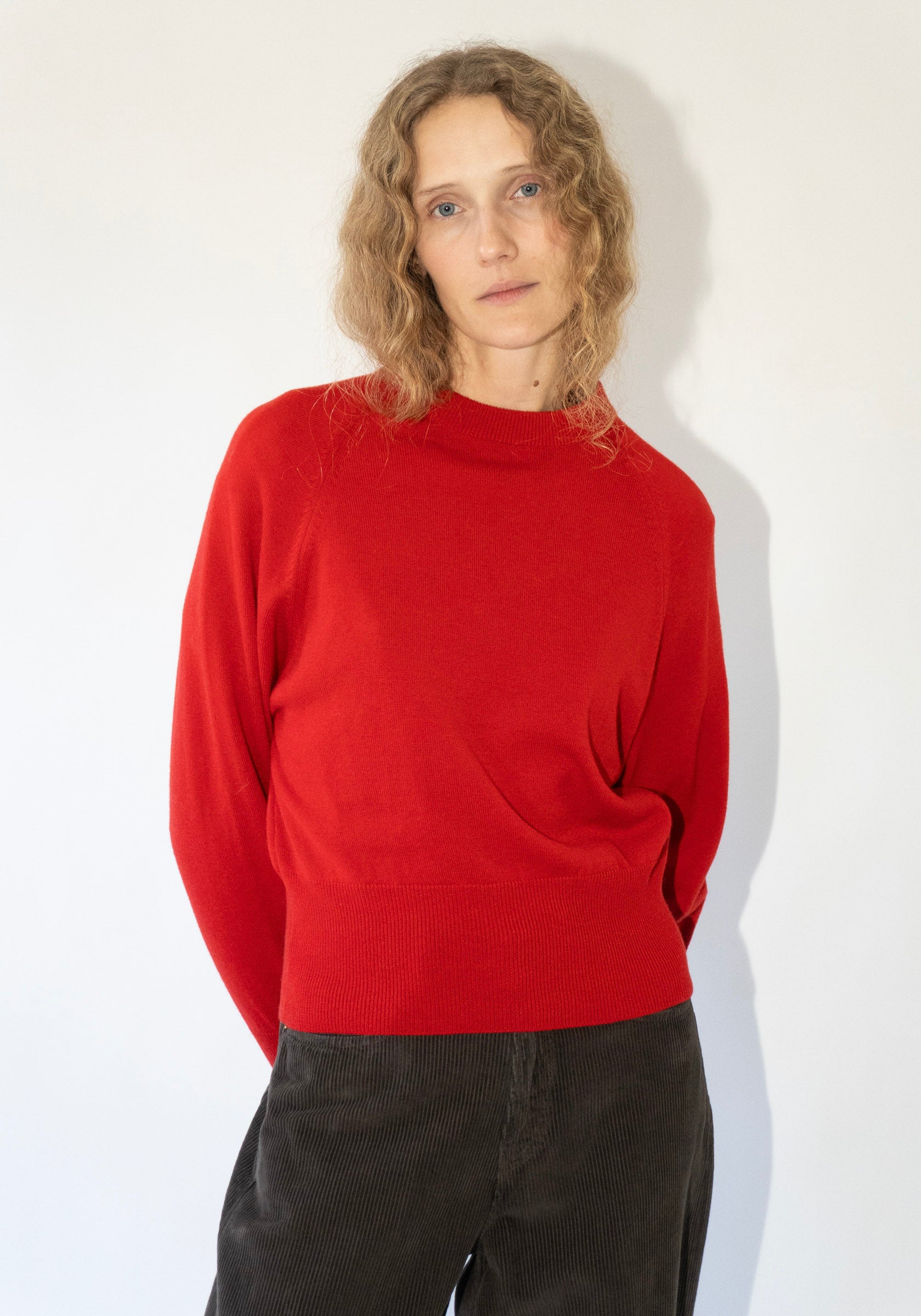 Person wearing a red sweater and black pants against a white background